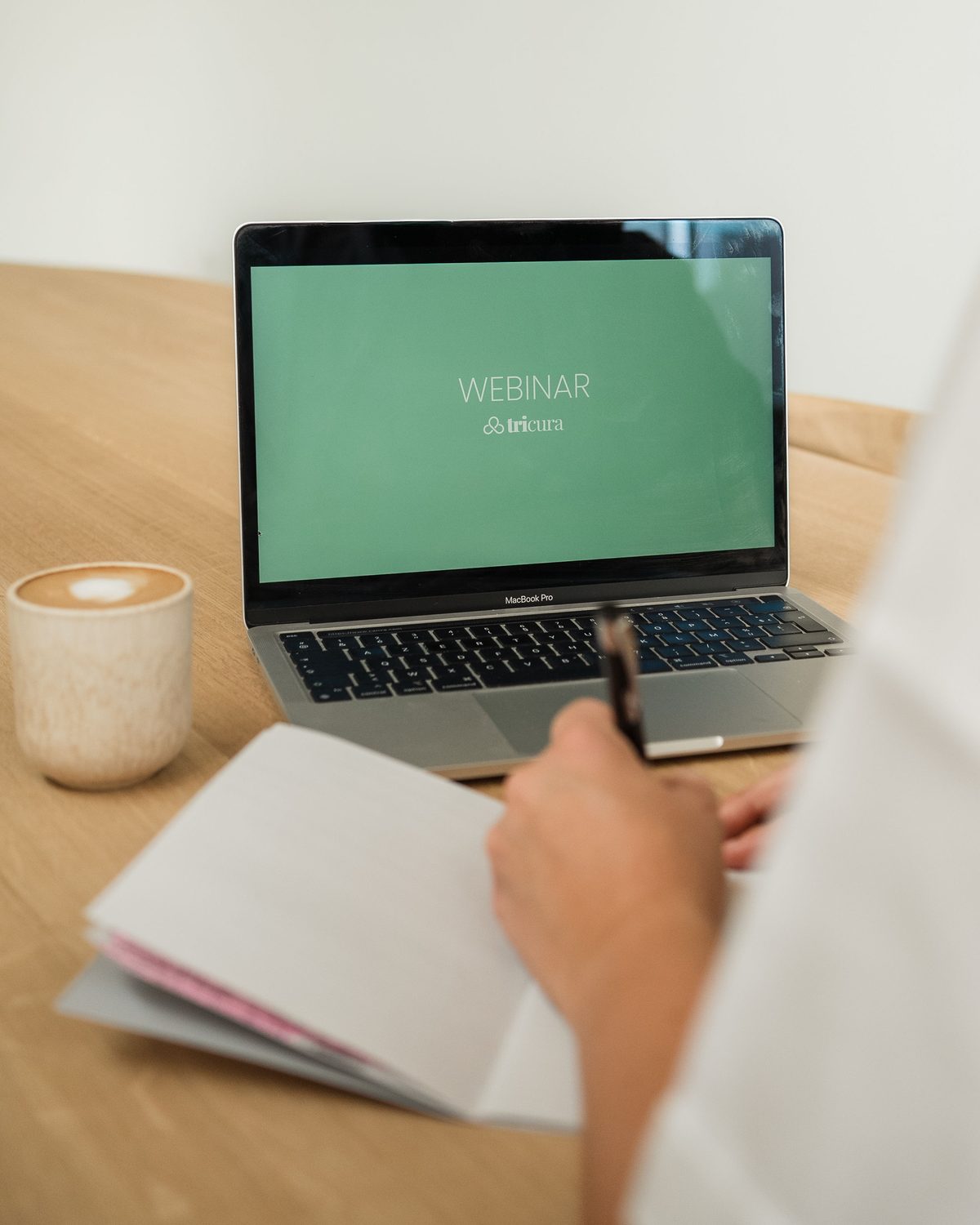 Laptop met een webinar van Tricura, ernaast koffie en notities