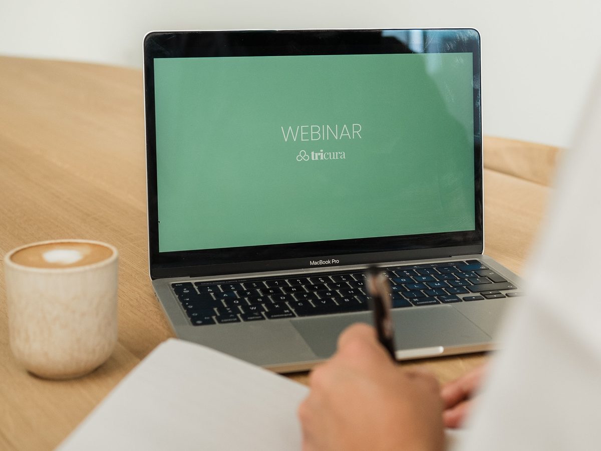 Laptop met een webinar van Tricura, ernaast koffie en notities