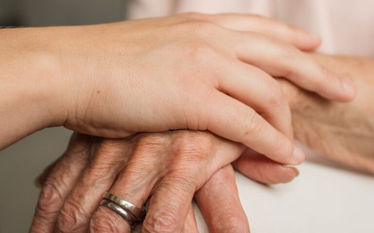 Een verzorgende hand op de hand van een oudere patient